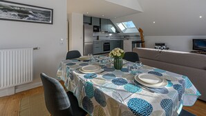 Una cocina moderna con tragaluces, un comedor con mesa dispuesta para cuatro personas y una sala de estar con sofá y televisor.