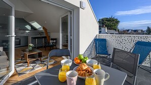 Un área de comedor exterior moderna con una mesa dispuesta para el desayuno, incluyendo croissants y jugo de naranja.