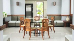 A dining area with a round table and six wooden chairs, a sofa, and a small side table with a vase. - Nava Magnolia Hotel (Bandung)
