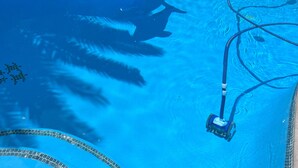 Una piscina con un limpiafondos automático y un objeto con forma de delfín flotando en el agua.