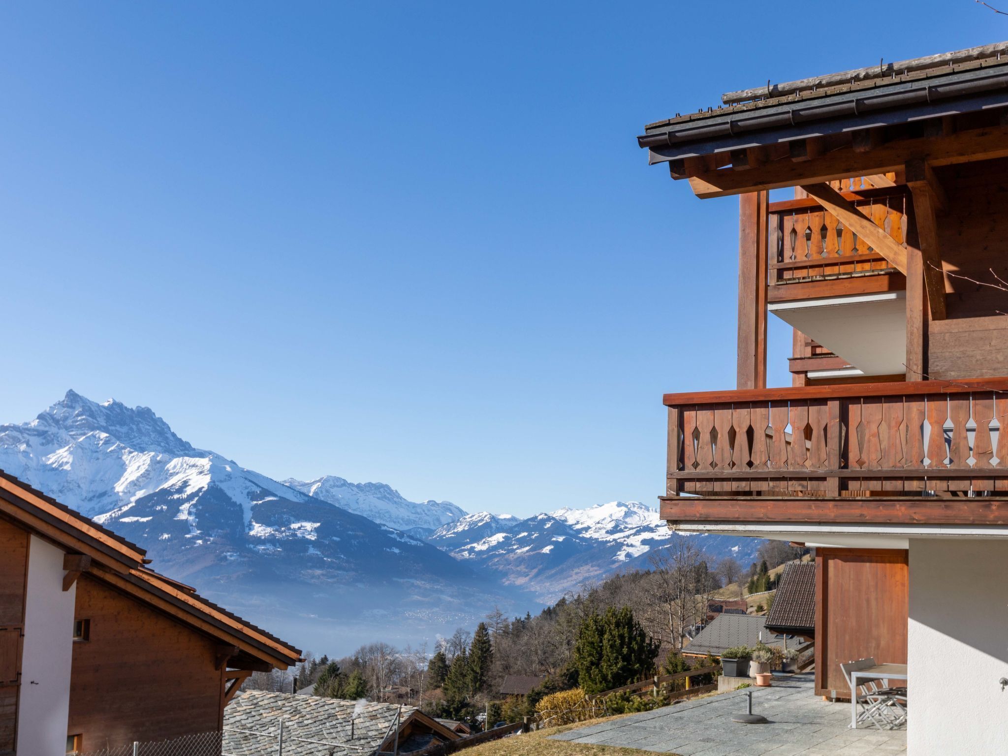 Un chalet de montagne avec des fondations en pierre, un balcon en bois et une vue sur des montagnes enneigées.