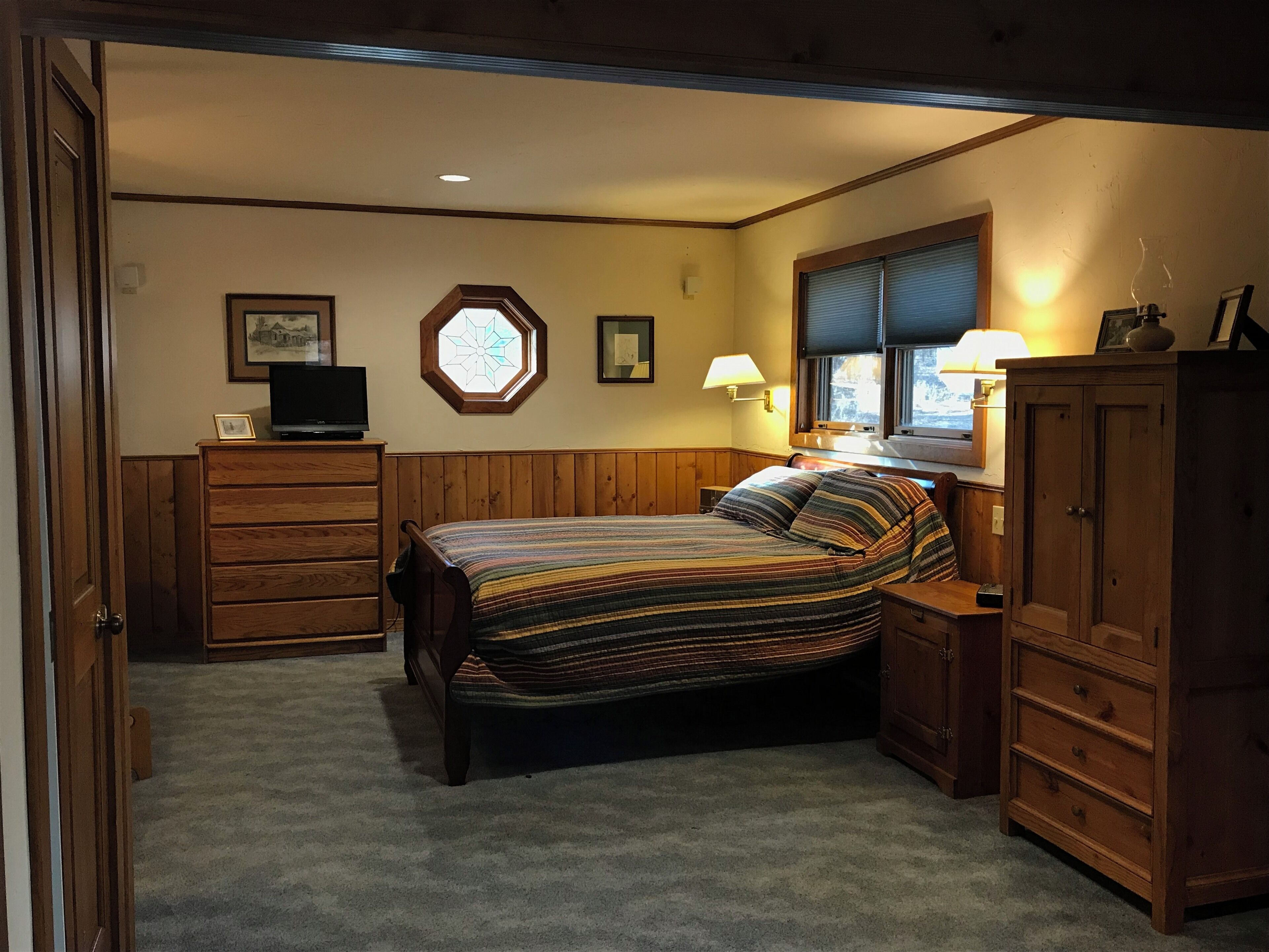 A bedroom with a bed, wooden dresser, and a television on a dresser.