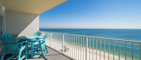 Un balcon avec des chaises turquoise, une vue sur l’océan et une balustrade blanche.