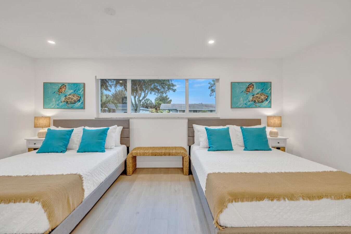 Habitación doble con dos camas, cada una con ropa de cama blanca y almohadas azules, un banco en el centro y obras de arte en las paredes.
