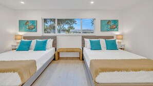 Quarto duplo com duas camas, cada uma com roupa de cama branca e almofadas azuis, um banco no centro e obras de arte nas paredes.