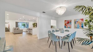 Uma sala de jantar moderna com uma mesa branca e cadeiras azuis, um candelabro e quadros abstratos na parede.