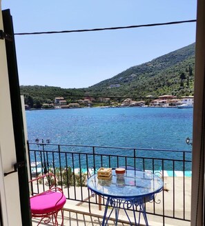 A balcony with a table and chairs overlooking a body of water and a hilly landscape.