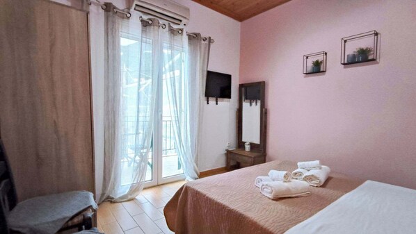 A bedroom with a bed, a chair, a window with curtains, a bedside table, and a wall-mounted TV.