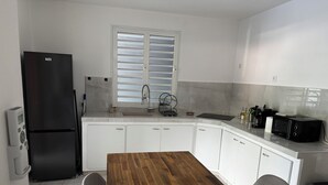 A modern kitchen with white cabinets, a wooden dining table, and a black refrigerator. - Comfortable family home between waterfalls and heavenly beaches (Petit-Bourg)