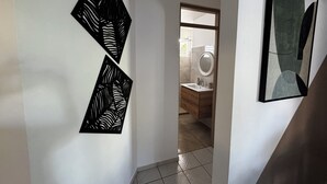 A hallway with two black wall art pieces, a wooden door leading to a bathroom, and a framed abstract painting on the right wall. - Comfortable family home between waterfalls and heavenly beaches (Petit-Bourg)