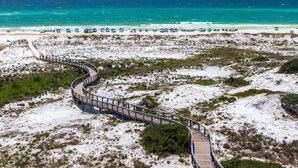 A wooden boardwalk leading to a beach with umbrellas and people.