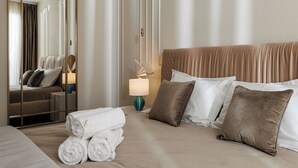 Ett hotellrum med en säng, ett sängbord med en lampa, en spegel och en väl bäddad säng med handdukar och kuddar.