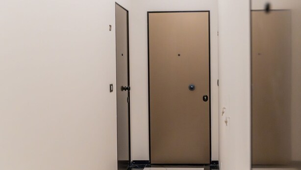 Un pasillo con una puerta cerrada, un interruptor de luz y suelo de mármol.