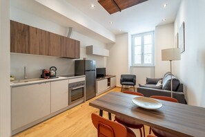 A modern kitchen with wooden cabinets, a dining table with orange chairs, a gray sofa, and a window with blinds. - Elegant 49 sqm apartment in the prestigious Palazzo Machiavelli, located in the heart of Trieste. Perfect for 4 guests, it is situated on the second floor of a building with an elevator (not suitable for disabled individuals). The location is excellent,  (Trieste)