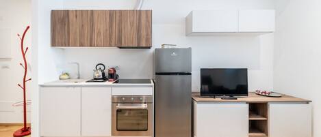 A compact kitchen with a built-in oven, a refrigerator, a coffee maker, and a television on a wooden counter.