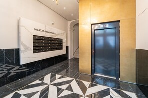 Un vestíbulo moderno con pared de mármol, piso con diseño geométrico y un ascensor azul.