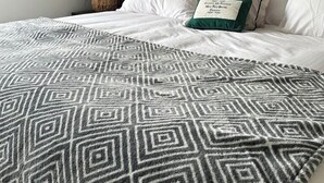 Een moderne slaapkamer met een gestoffeerd hoofdeinde, een gebreid plaid en een potplant.