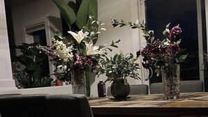 Een eettafel met stoelen, een vaas met bloemen en een raam op de achtergrond.