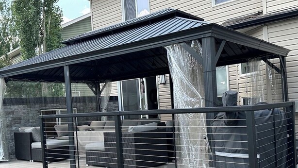 Een overdekt terras met een metalen hek, stenen trappen en een stenen muur.