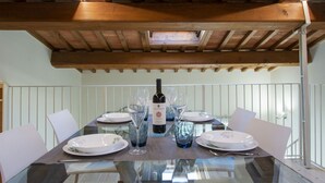 Mesa de comedor lista para seis, con una botella de vino, copas y platos.