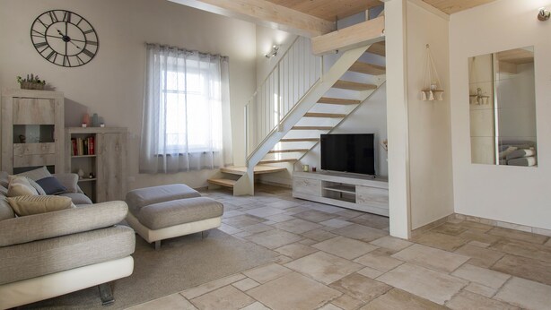 Un salón espacioso con una escalera, un televisor y un reloj en la pared.