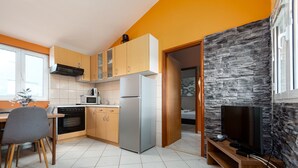 A modern kitchen with wooden cabinets, a refrigerator, an oven, and a dining area with a chair.