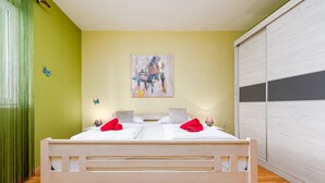 Un lit bien fait, avec du linge de lit blanc et des serviettes rouges, un tableau accroché au mur et un rideau vert sur le côté gauche.