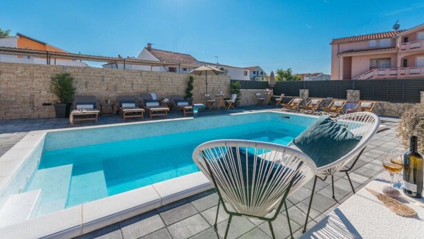 A swimming pool with lounge chairs and a stone wall. - Apartment Julia A5, 2+2 (Biograd na moru)