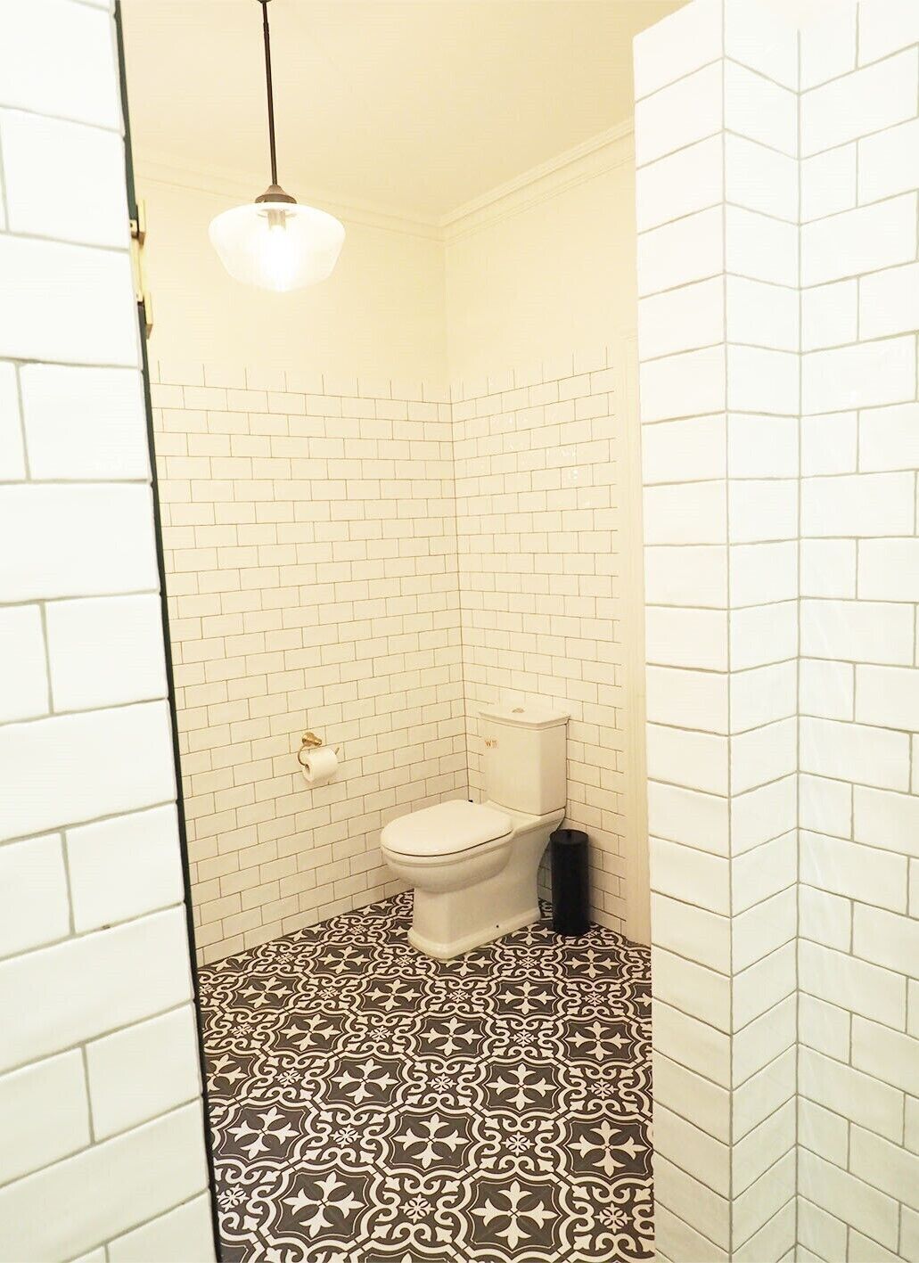 A small, narrow bathroom with a white toilet, a patterned floor, and a hanging light fixture.