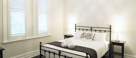 A bedroom with a large bed, dark wood flooring, a chandelier, and two bedside tables.