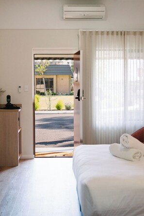 A hotel room with a bed, a desk, and a view of the street and building outside.