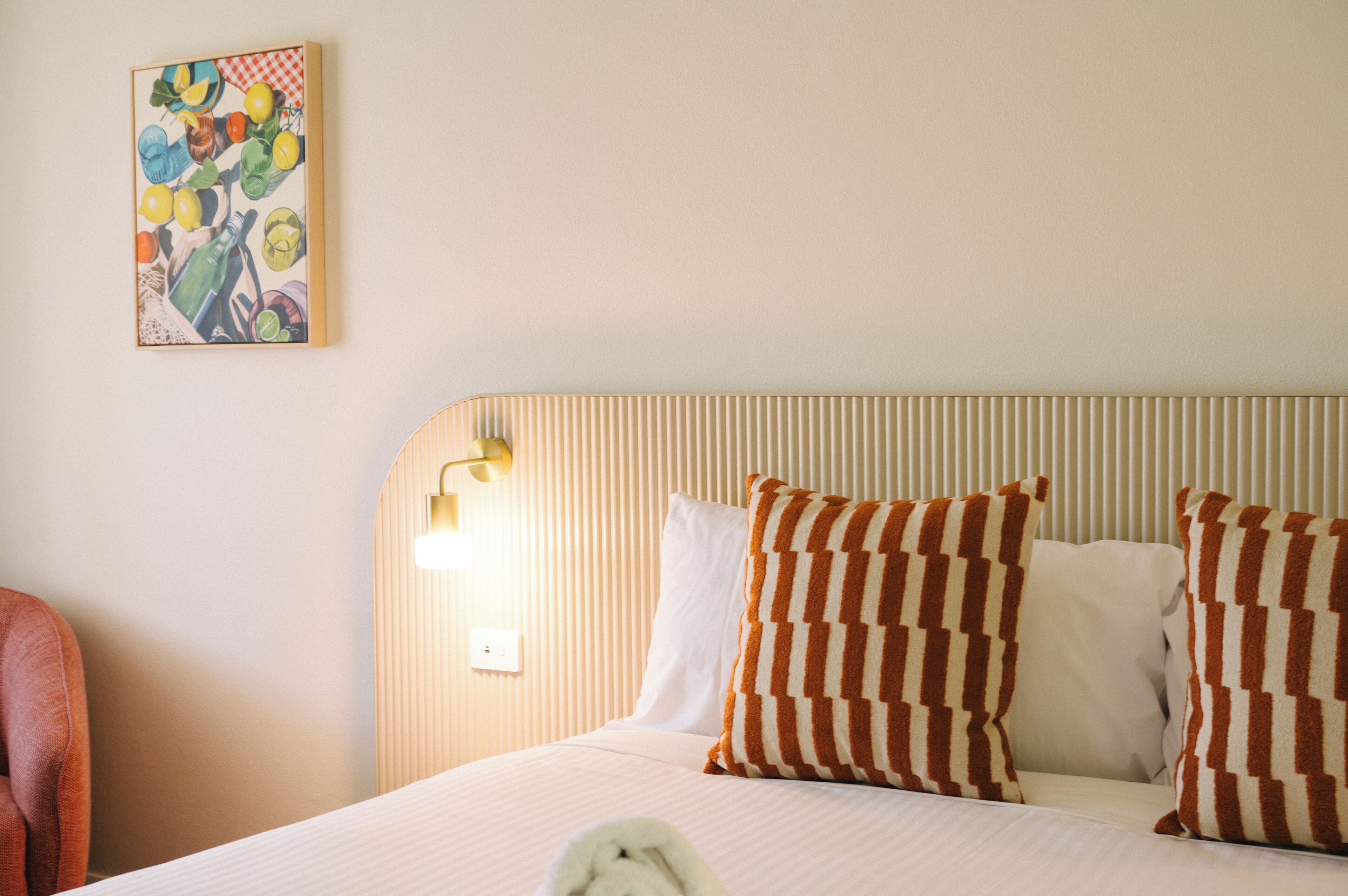 A hotel room with a bed, striped headboard, and a painting on the wall.