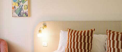 A hotel room with a bed, striped headboard, and a painting on the wall.