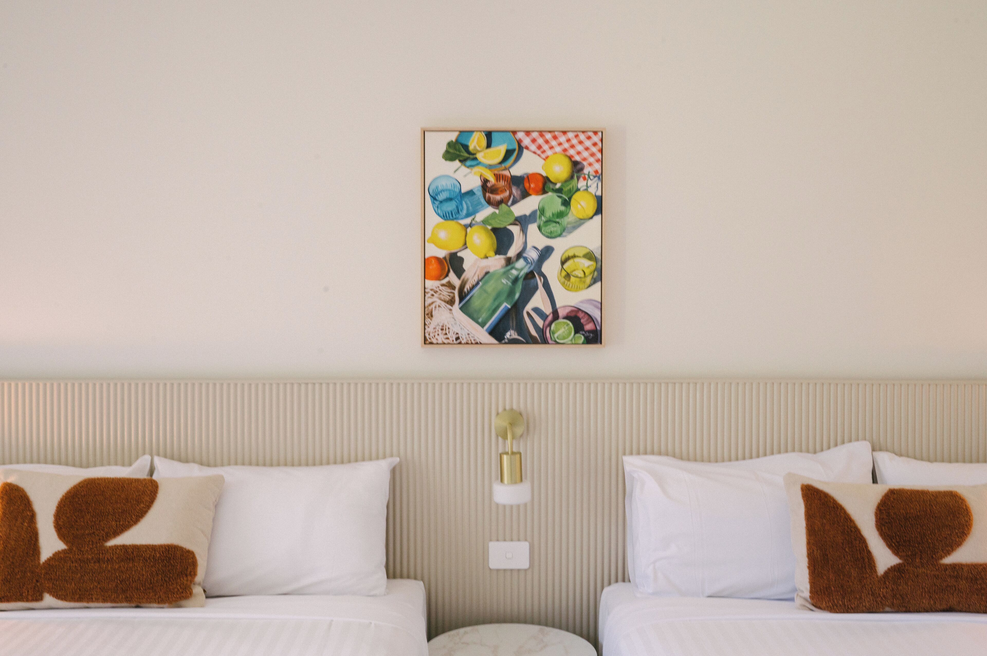 A hotel room with two beds, a wall-mounted artwork, and a round nightstand.