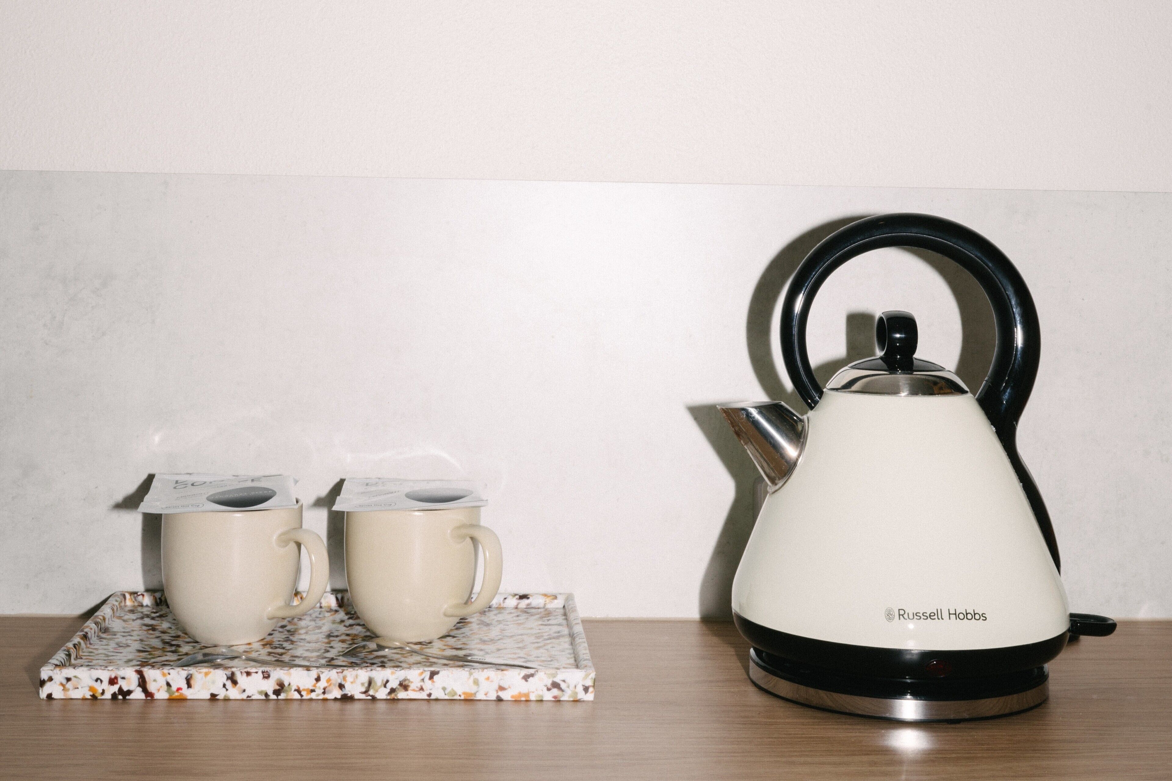 A white kettle with a black handle and a lid on a white base, placed on a wooden table.