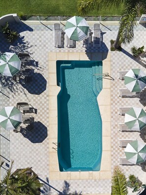 An aerial view of a swimming pool surrounded by checkered tiles, with multiple lounge chairs and umbrellas. - The Timothee Resort (Busselton)