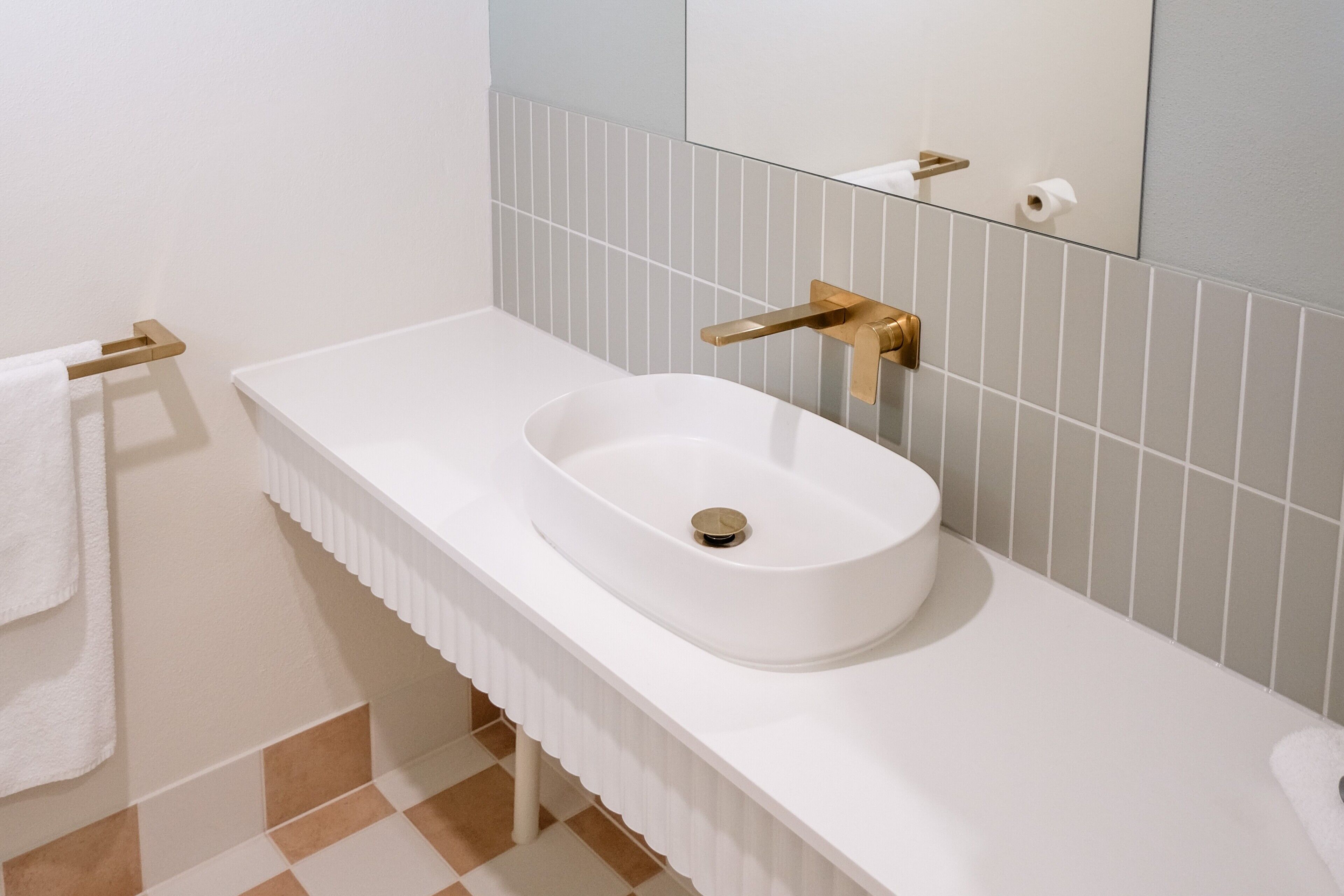 Un baño con lavamanos blanco, grifo dorado y un perchero para toallas.