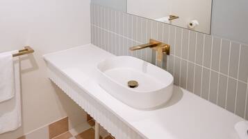 Un baño con lavamanos blanco, grifo dorado y un perchero para toallas.