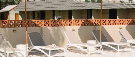 A pool area with lounge chairs and umbrellas, a pool with clear water, and a building with a tiled roof in the background.