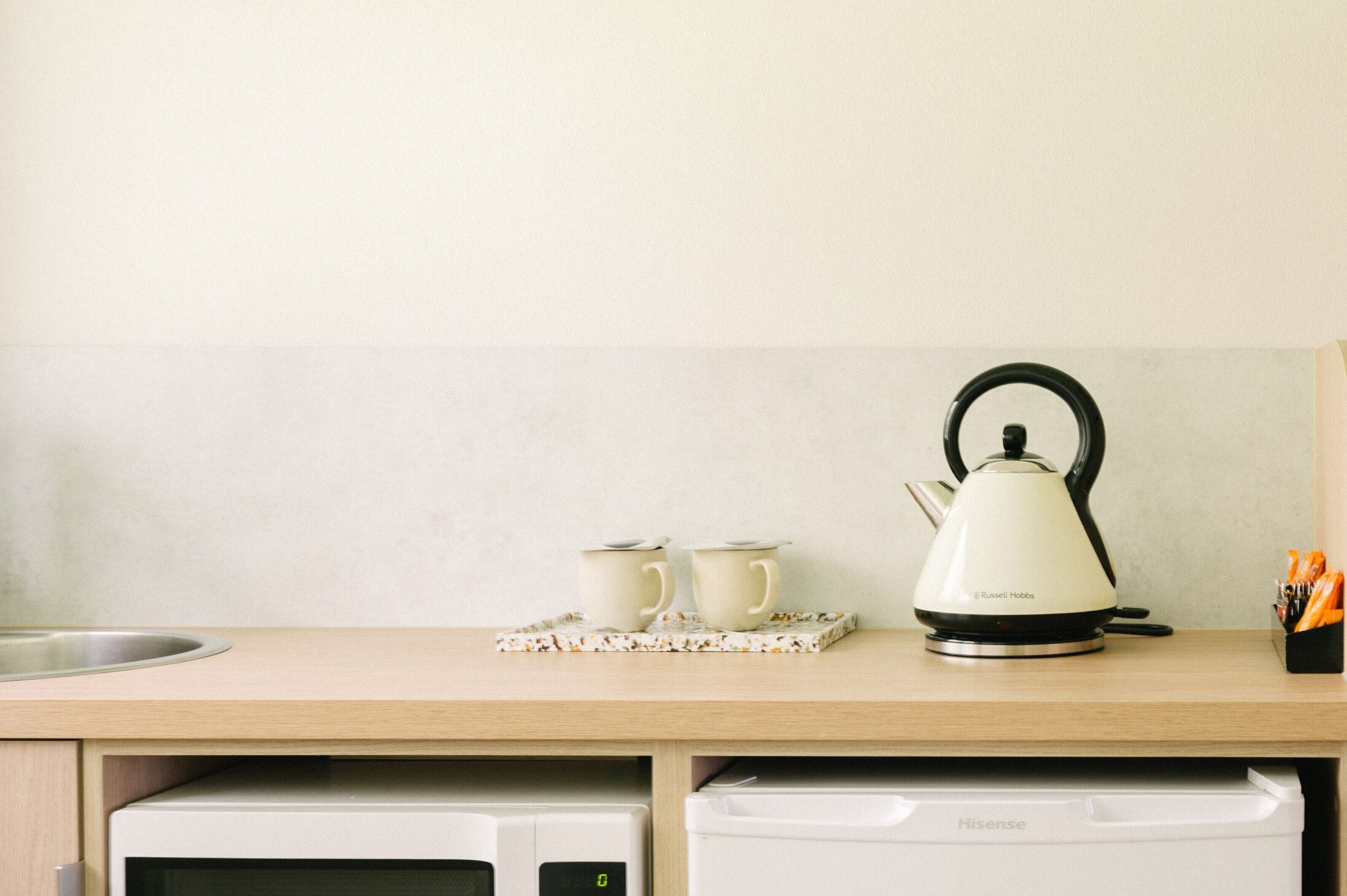A kitchen counter with a kettle, two cups, and a tray.