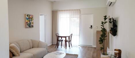 Una sala de estar con sofá, mesa de centro, mesa de comedor con sillas y una planta.