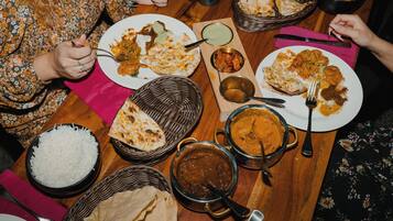 Een eettafel met diverse gerechten, zoals rijst, curry en platbrood, wat een maaltijdsetting doet vermoeden.