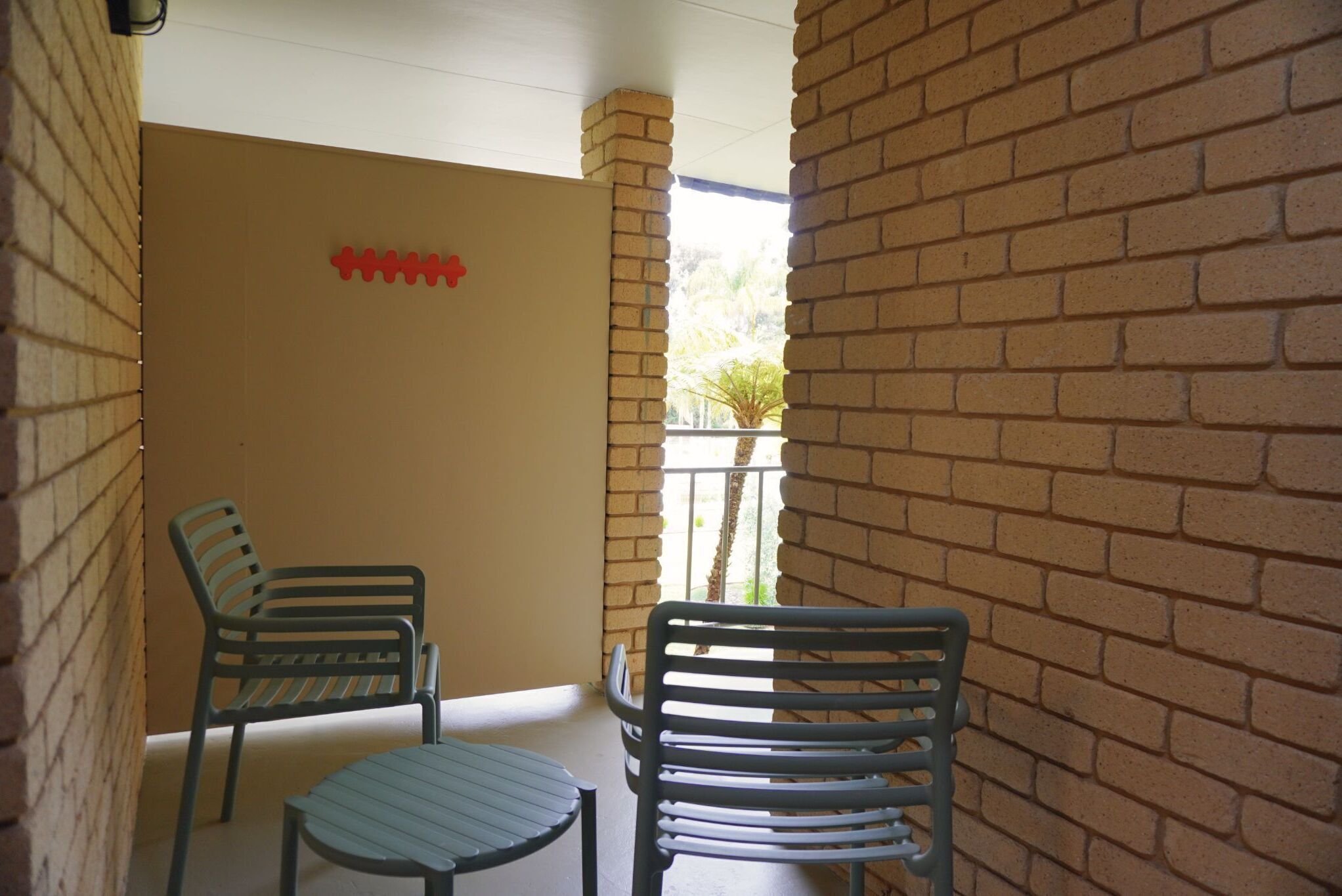 Un balcon avec deux chaises en métal et une petite table, des murs en briques et un élément décoratif rouge sur le mur.