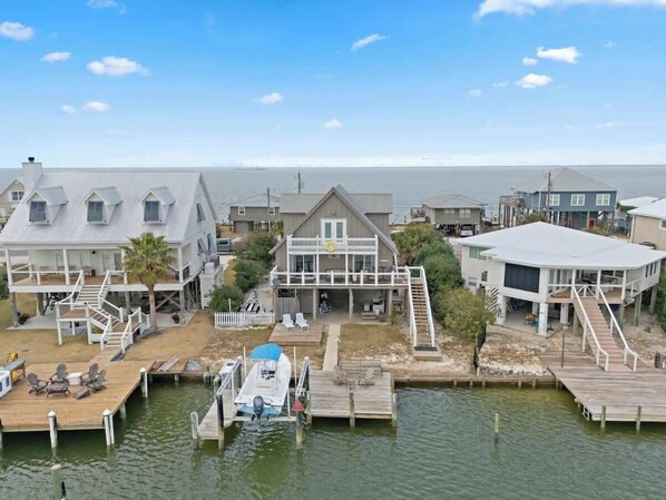 A waterfront property with multiple houses connected by docks, featuring outdoor seating areas and a boat docked at the center.