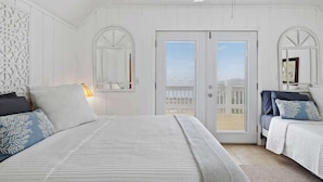 A bedroom with a large bed, two bedside tables, a ceiling fan, and a door leading to a balcony.