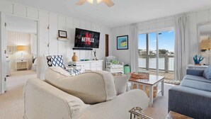 A living room with a large flat-screen TV, a ceiling fan, and a view of the outside.