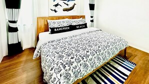 A bedroom with a wooden bed, black and white patterned bedding, a framed marine life poster, and a black pillow with "BANCHUEN BEACH" text. - Hello Banchuen Beach (Khlong Yai)