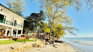 A beachfront property with a modern building, a sandy beach, and a row of surfboards. - Hello Banchuen Beach (Khlong Yai)