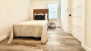 Un dormitorio con cama, una mesita de noche pequeña, una ventana y un ventilador de techo.