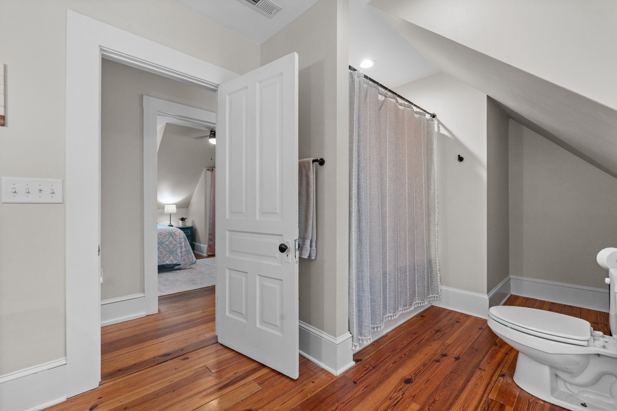 A bathroom with a wooden floor, a white toilet, and a shower curtain.